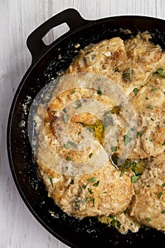 Homemade Italian Chicken Piccata in a cast iron pan on a white wooden table, top view. Overhead, from above, flat lay