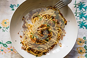 Homemade italian pasta dish known as `pasta con le sarde` on table cloth, made with spaghetti, sardines, parsley, pine nuts and b