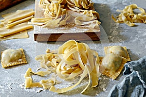 Homemade italian pasta, ravioli, fettuccine, tagliatelle on a wooden board and on a blue background.