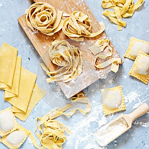 Homemade italian pasta, ravioli, fettuccine, tagliatelle on a wooden board and on a blue background. The cooking process