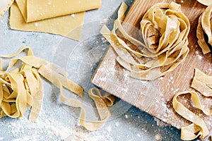 Homemade italian pasta, ravioli, fettuccine, tagliatelle on a wooden board and on a blue background. The cooking process