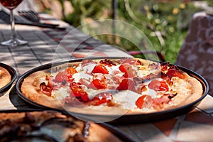 Homemade Italian pizza with tomato, cheese and ham in the plate on tile table in the garden. Selective focus.