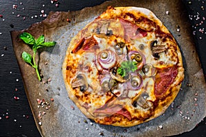Homemade Italian pizza topped with ham, cheese, onion, mushroom, olive and tomato