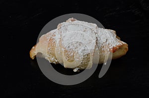 Homemade jam bun sprinkled with powdered sugar close-up on a dark wooden surface