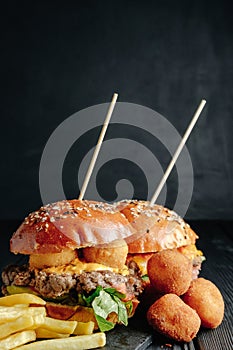 Homemade juicy burgers on wooden board, cheese balls and French fries