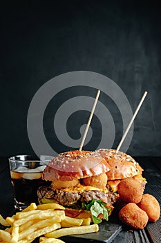 Homemade juicy burgers on wooden board, cheese balls with French fries and glass of cola