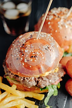 Homemade juicy burgers on wooden board, cheese balls with French fries and glass of cola
