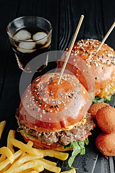 Homemade juicy burgers on wooden board, cheese balls with French fries and glass of cola