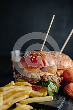 Homemade juicy burgers on wooden board, cheese balls with French fries and glass of cola