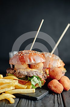 Homemade juicy burgers on wooden board, cheese balls with French fries and glass of cola