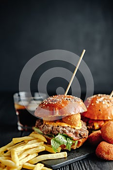 Homemade juicy burgers on wooden board, cheese balls with French fries and glass of cola