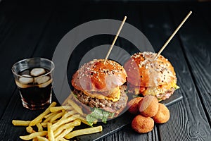 Homemade juicy burgers on wooden board, cheese balls with French fries and glass of cola