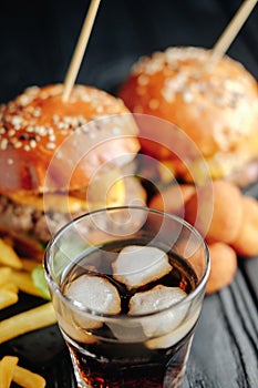 Homemade juicy burgers on wooden board, cheese balls with French fries and glass of cola