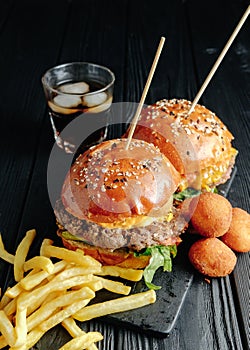 Homemade juicy burgers on wooden board, cheese balls. with French fries and glass of cola. top view