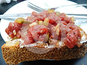 Homemade juicy tartare lies on crispy grilled piece of bread. Chopped raw meat with onions and pickles laid out on butter spread