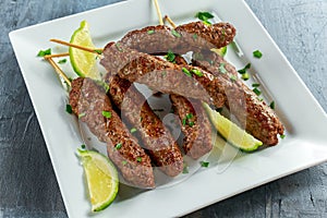Homemade Kofta kebabs on skewers with lime and parsley on white plate photo