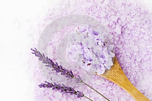 Homemade lavender body scrub in wooden spoon on lavender bath salt background. Top view, copy space. SPA concept