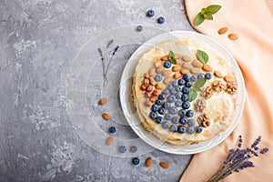 Homemade layered Napoleon cake with milk cream. Decorated with blueberry, almonds, walnuts, hazelnuts, mint on a gray concrete