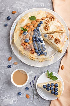 Homemade layered Napoleon cake with milk cream. Decorated with blueberry, almonds, walnuts, hazelnuts, mint on a gray concrete