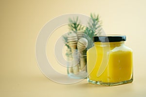 Homemade lemon curd in small glass jar with black lid on yellow background