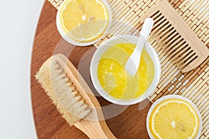 Homemade lemon fruit scrub bath salt, foot soak, facial or hair mask in a small white bowl and wooden hairbrush. Natural beauty