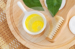 Homemade lemon fruit scrub mask in a small white bowl and wooden body brush. Natural beauty treatment and spa recipe. Top view
