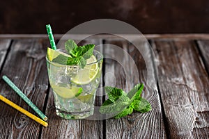 Homemade lemonade in a glass with lime, mint leaves, straw and ice on a dark wooden table. Summer refreshing drink. Selective