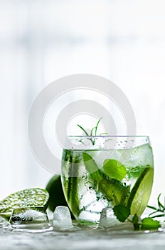 Homemade lime lemonade with cucumber, rosemary and ice, white background. Cold beverage for hot summer day. Copyspace