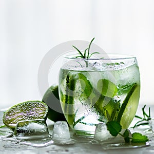 Homemade lime lemonade with cucumber, rosemary and ice, white background. Cold beverage for hot summer day. Copyspace