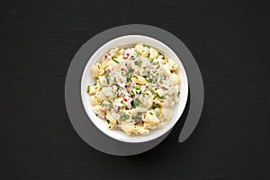 Homemade Macaroni Salad in a white bowl on a black background, top view. Flat lay, overhead, from above