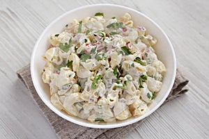 Homemade Macaroni Salad in a white bowl on a white wooden background, side view. Close-up