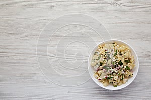 Homemade Macaroni Salad in a white bowl on a white wooden background, top view. Flat lay, overhead, from above. Space for text
