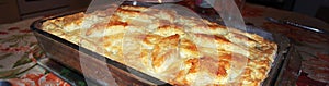 Homemade meat pie with golden crust, decorated with ornament of dough, cools in glass baking dish, in which it was prepared