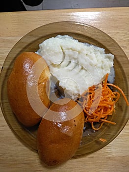 Homemade meat pies, mashed potato, grated carrots on the brown plate close-up