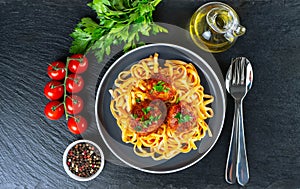 Homemade meatballs with tomato sauce and spices served in black pan on black slate background