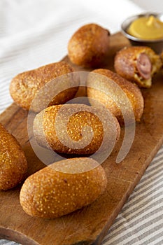 Homemade Mini Corn Dogs on a rustic wooden board on cloth, side view