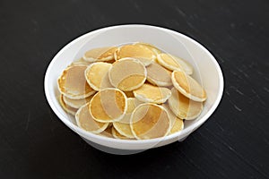 Homemade Mini Pancakes Cereal in a white bowl on a black surface, side view