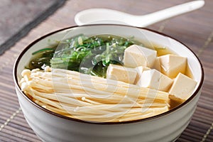 Homemade miso soup with tofu cheese, enoki mushrooms, wakame seaweed close-up in a bowl. Horizontal