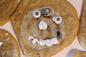 A homemade, misshapen chocolate chip cookie with a face created out of candy and marshmallow bits.