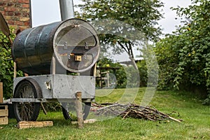 Homemade mobile pizza oven from an old metal barrel on a recycled chassis in a garden, fire in the combustion chamber and firewood