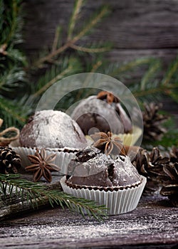 Homemade muffins with cinnamon and star anise surrounded by decorations and Christmas tree branches on wooden table