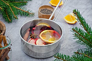 Homemade mulled wine with apple, orange, ginger, cinnamon, cardamom and star anise in a saucepan on a gray background.