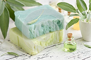 Homemade natural organic soap bars, bottle of essential sage oil and fresh green sage leaves on white table