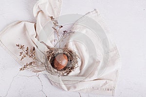 Homemade naturally colored egg in a nest on a napkin and dried flowers on the table top view