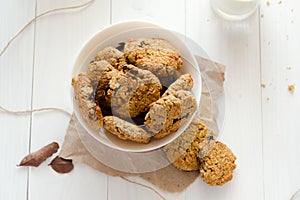 Homemade oatmeal cookies with raisins and prunes with jug and glass of milk on white wooden background. No sugar, no flour