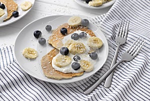 Homemade oatmeal pancakes with yogurt, fresh blueberry and banana at white wooden background