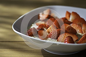 Homemade oatmeal porridge bowl with sliced strawberries on table in morning sunlight