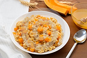 Homemade oatmeal porridge with seasonal autumn pumpkin in a white plate on a dark wooden background. autumn composition with wheat