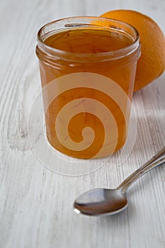 Homemade orange marmelade in glass jar on a white wooden background, side view