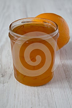 Homemade orange marmelade in glass jar on a white wooden background, side view. Closeup